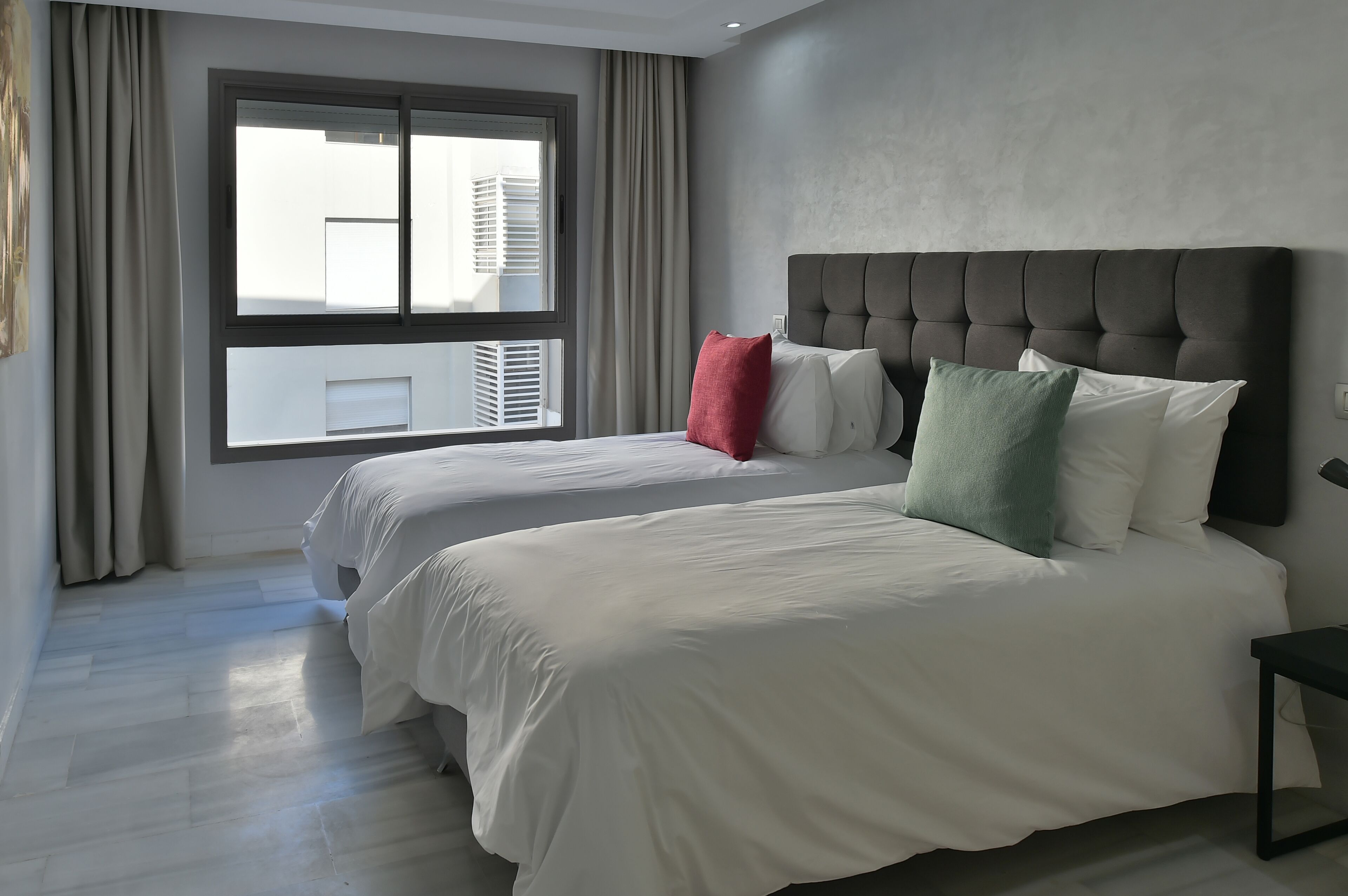 Een hotelkamer met twee bedden, een groot raam met gordijnen, een grijze hoofdeinde en een modern design.
