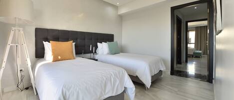 Una habitación de hotel moderna con dos camas, un ventanal grande y un pasillo que conduce a otra habitación.