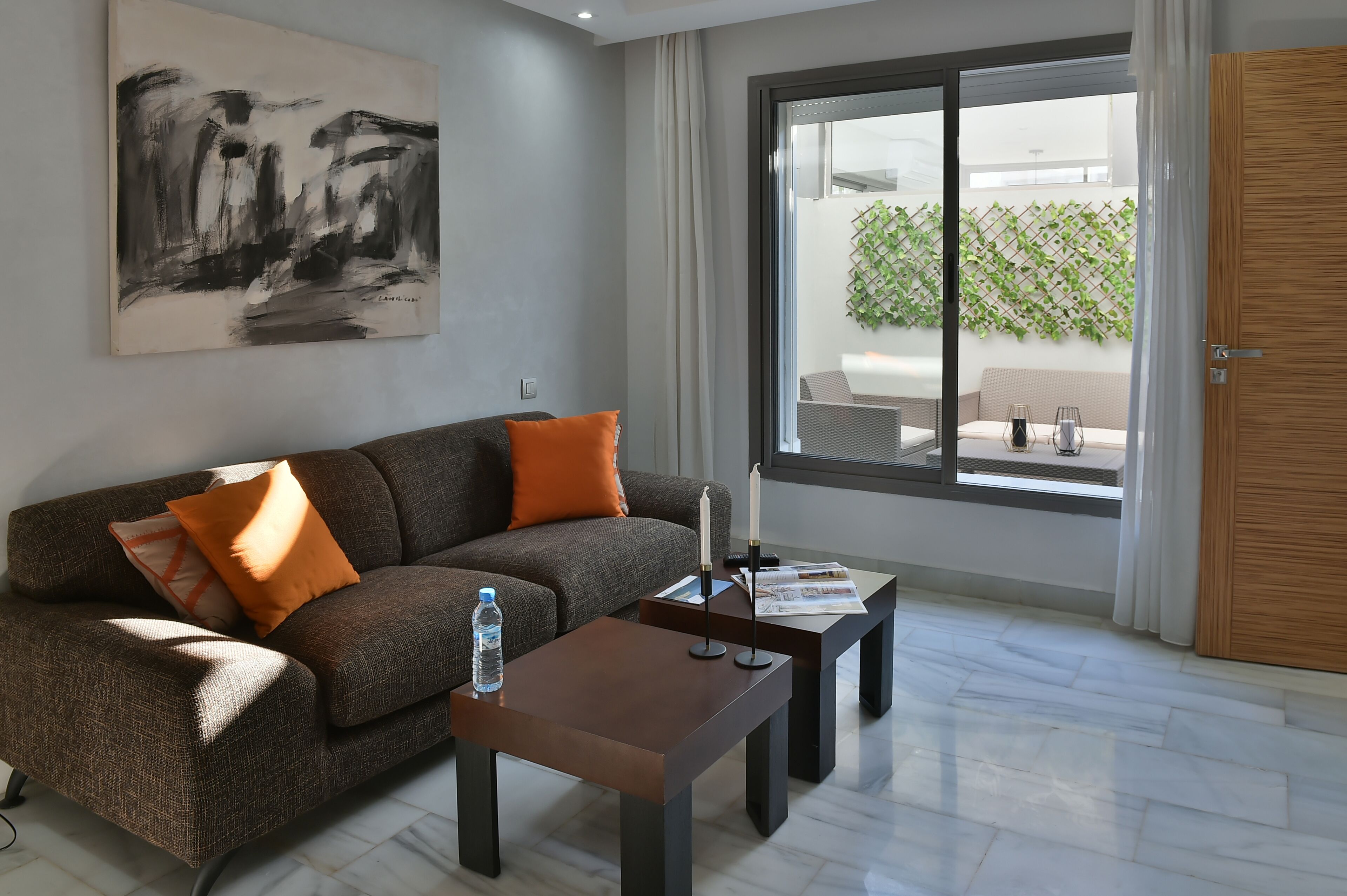 Un salon moderne avec un canapé gris, des coussins orange, une table basse en bois et un grand tableau abstrait accroché au mur.
