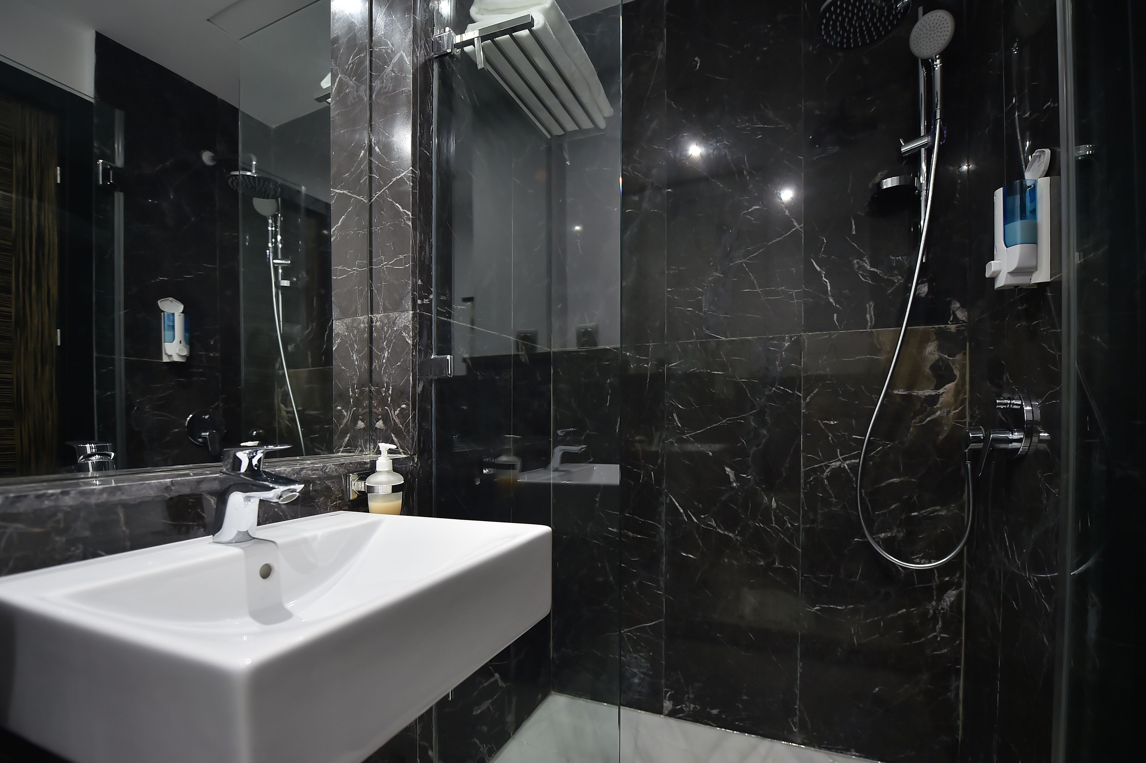 A modern bathroom with a white sink, a glass-enclosed shower, and marble walls.