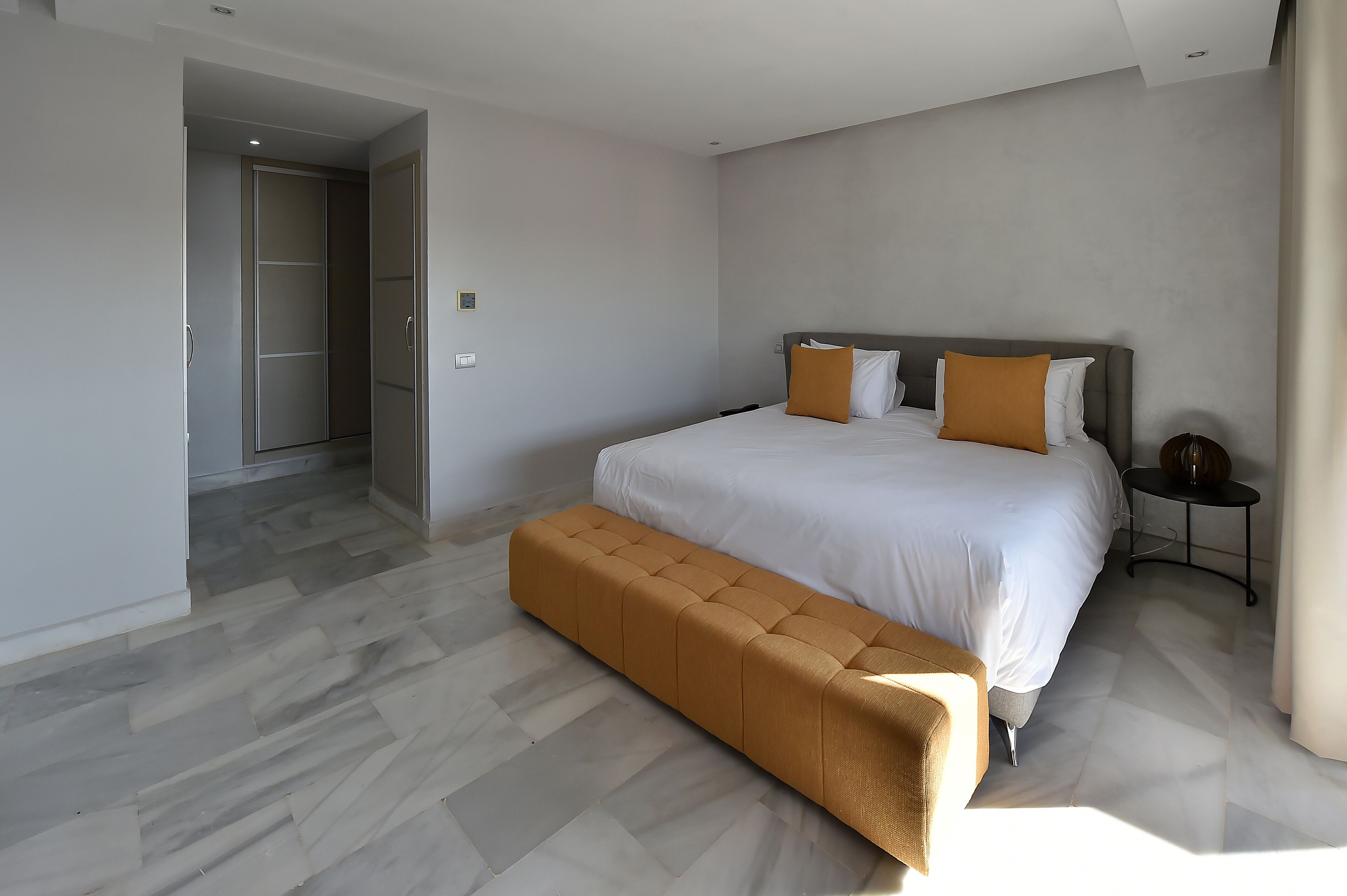 A modern hotel room with a large bed, a bench, and a small bedside table.