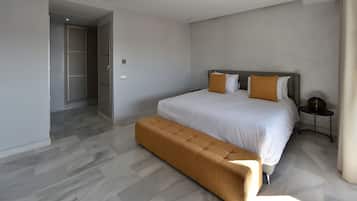A modern hotel room with a large bed, a bench, and a small bedside table.