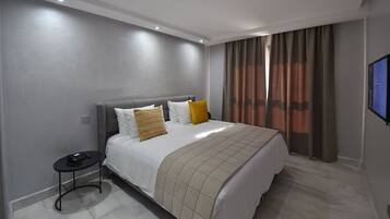 A modern hotel room with a large bed, a bedside table with a phone, and a TV on the wall.