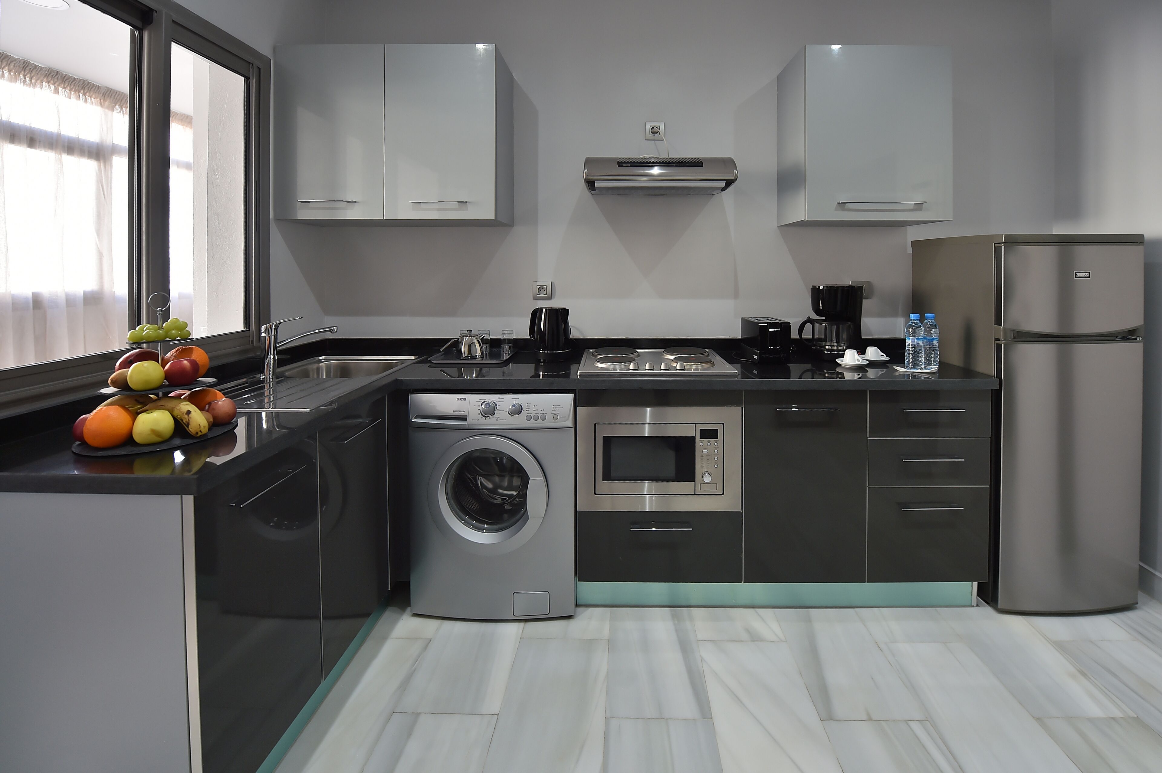 A modern kitchen with a washing machine, microwave, and refrigerator.