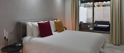 Habitación de hotel moderna con una cama grande, una mesita de noche con teléfono y vistas al exterior a través de una ventana.