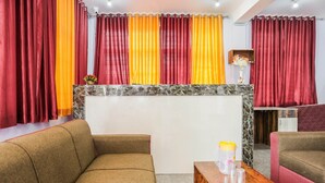 A hotel room with a sofa, a wooden table, and curtains in red and orange. - Oyo 43512 Bijaya Palace (Bhubaneshwar)