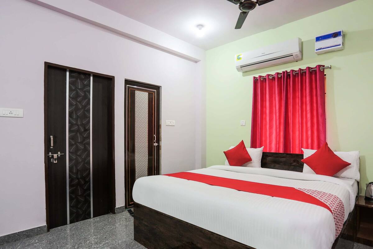 Une chambre d’hôtel avec un lit, des rideaux rouges, un climatiseur et un ventilateur de plafond.