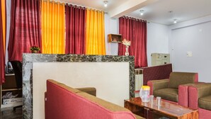 A hotel lobby with red and orange curtains, a marble reception desk, and seating areas with red and brown upholstered chairs. - Oyo 43512 Bijaya Palace (Bhubaneshwar)