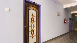 A hallway with a wooden door featuring a decorative glass panel, a fire extinguisher, and a purple wall. - Oyo 43512 Bijaya Palace (Bhubaneshwar)