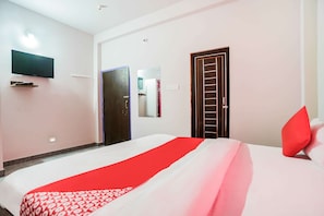 A hotel room with a bed, a TV mounted on the wall, a door, and a mirror.