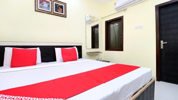 A hotel room with a bed, a bedside table, a mirror, and an air conditioning unit. - OYO 27650 Gian Residency (Amritsar)