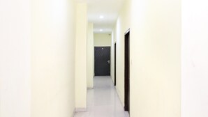A narrow hallway with cream-colored walls and a tiled floor, leading to a dark door at the end. - OYO 27650 Gian Residency (Amritsar)