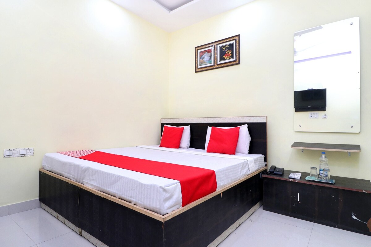 A hotel room with a bed, a bedside table, a mirror, and a wall-mounted shelf.