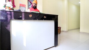 A reception desk with a man standing behind it, a whiteboard, and a framed picture on the wall. - OYO 27650 Gian Residency (Amritsar)