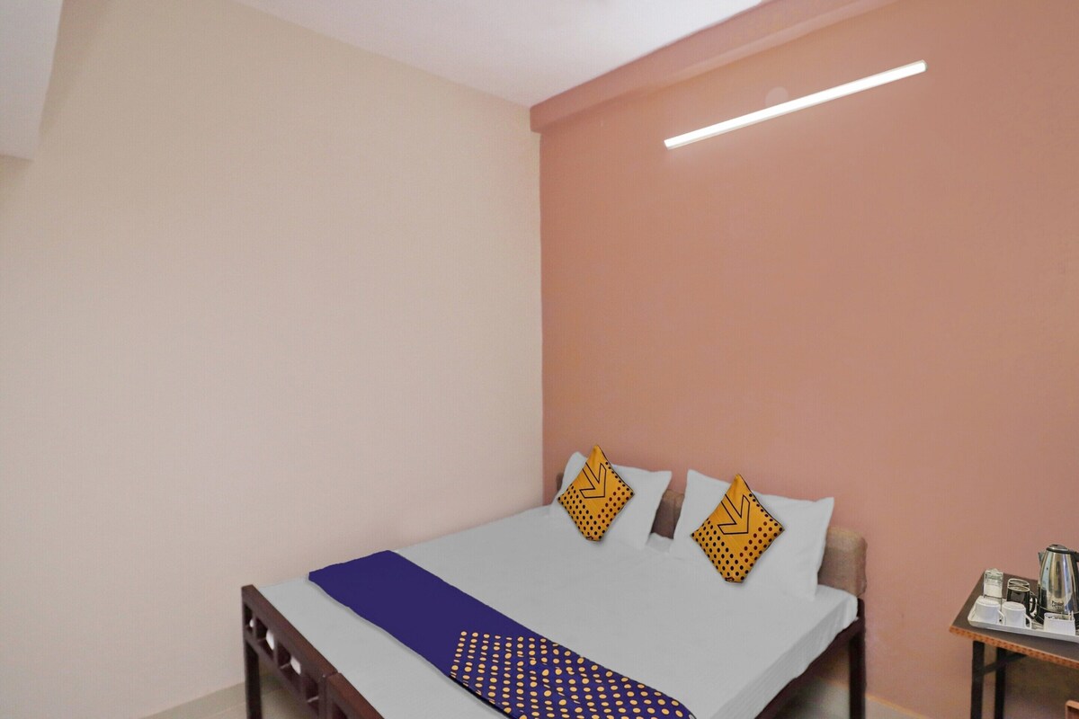 A neatly made bed with a blue and white bedspread, two decorative pillows, and a small table with a kettle and cups beside the bed.