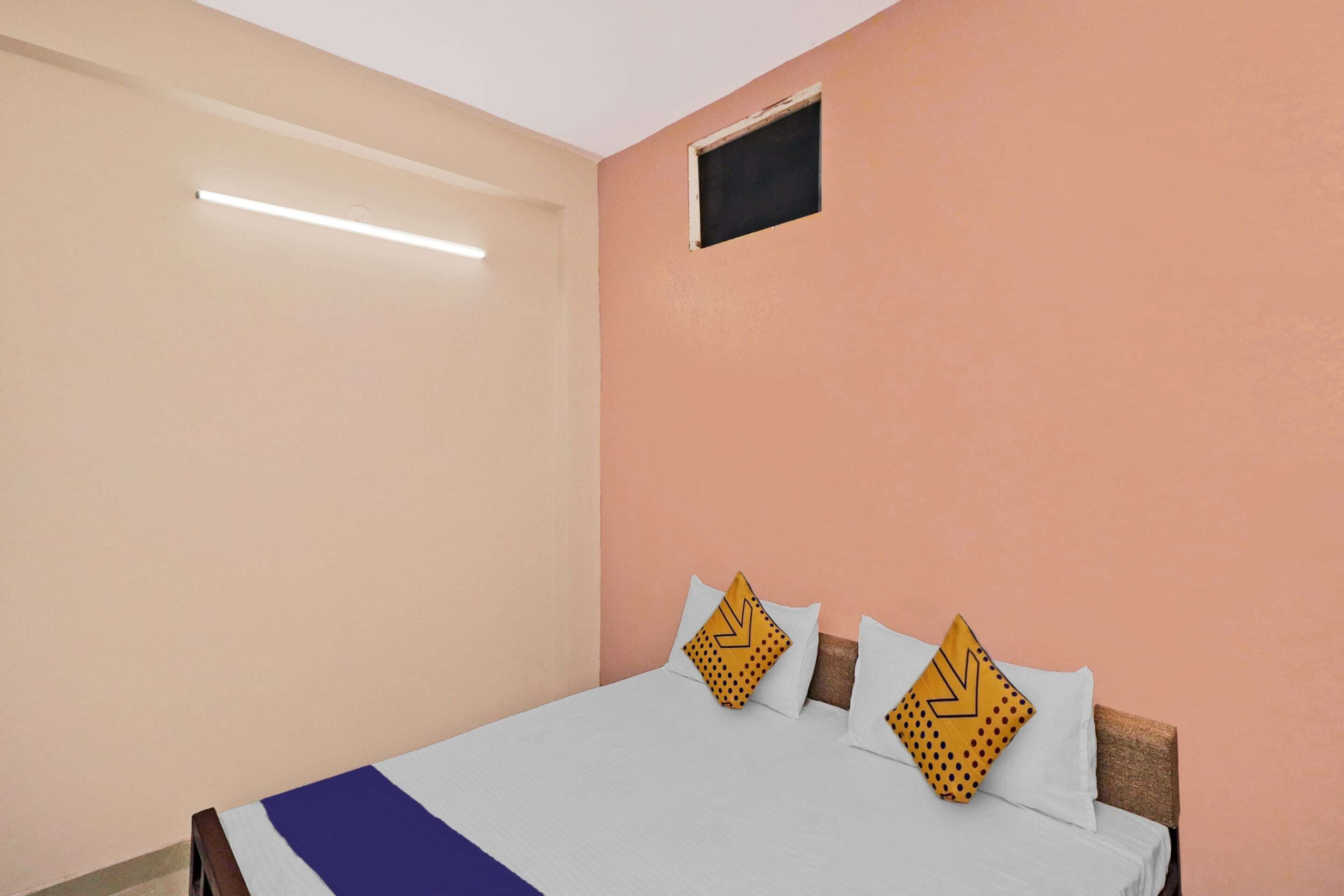A single bed with a white and blue bedspread, two pillows with yellow patterns, and a small window above the bed.
