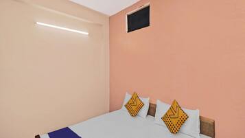 A single bed with a white and blue bedspread, two pillows with yellow patterns, and a small window above the bed.