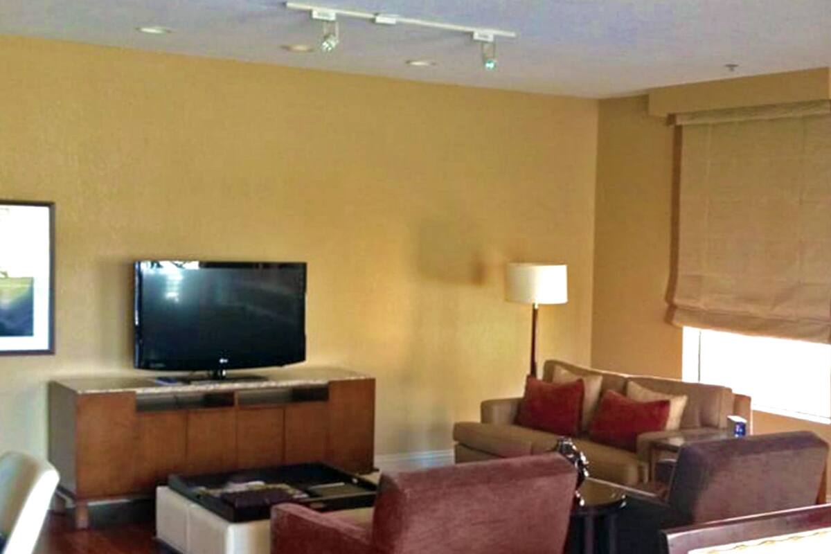 A hotel room with a wooden floor, a flat-screen TV on a wooden cabinet, a sofa, a chair, and a table.