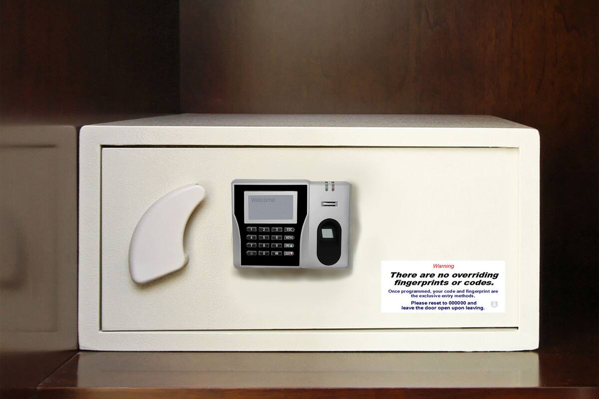 A white safe with a keypad and a card slot, and a warning sign about no overriding fingerprints or codes.