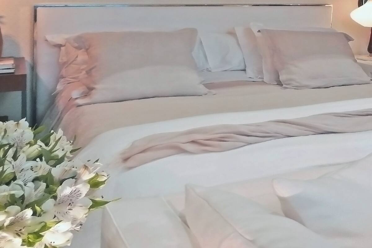 A bed with white bedding and pillows, a bedside table with a lamp, and a bouquet of flowers.