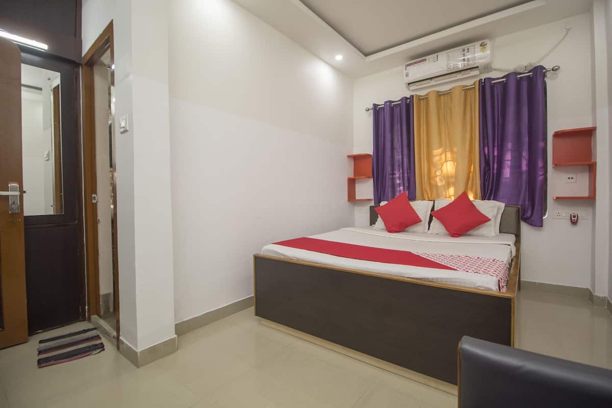 A bedroom with a bed, a door, a mirror, a window with curtains, and a wall-mounted air conditioner.