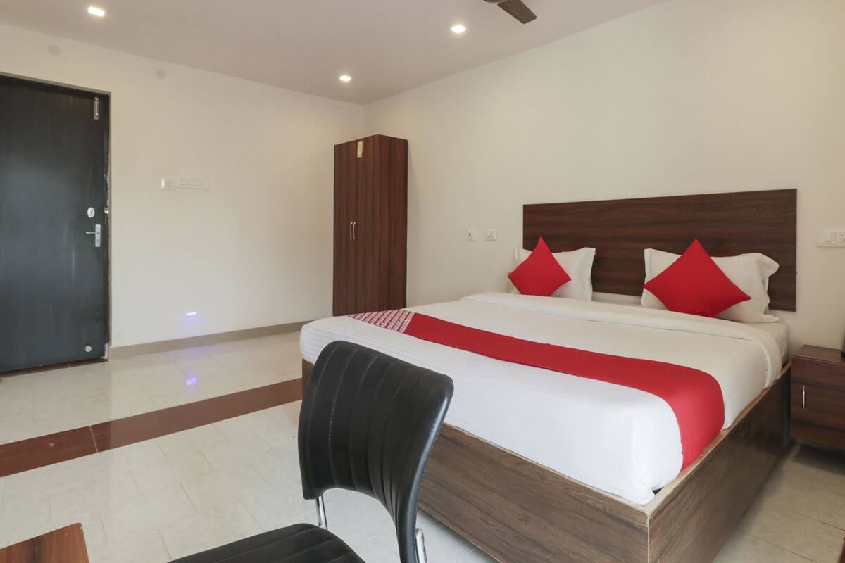 Une chambre d’hôtel avec un lit, une armoire en bois, un ventilateur de plafond et une chaise.