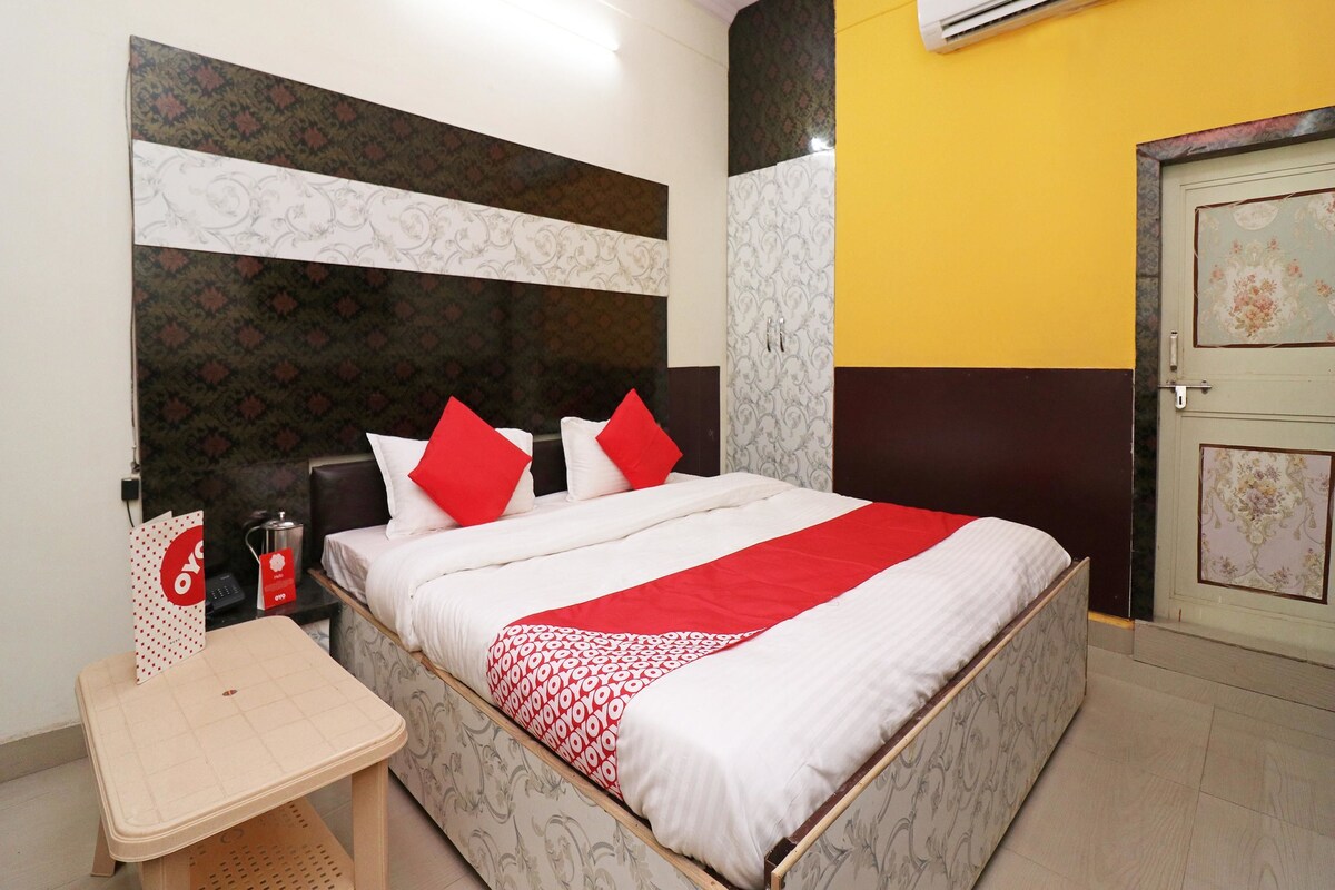 A neatly arranged hotel room with a bed, bedside table, and an air conditioning unit.