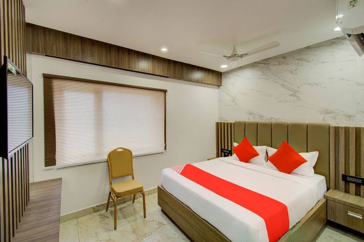 Een hotelkamer met een bed, een stoel, een nachtkastje, een plafondventilator en een raam met jaloezieën.