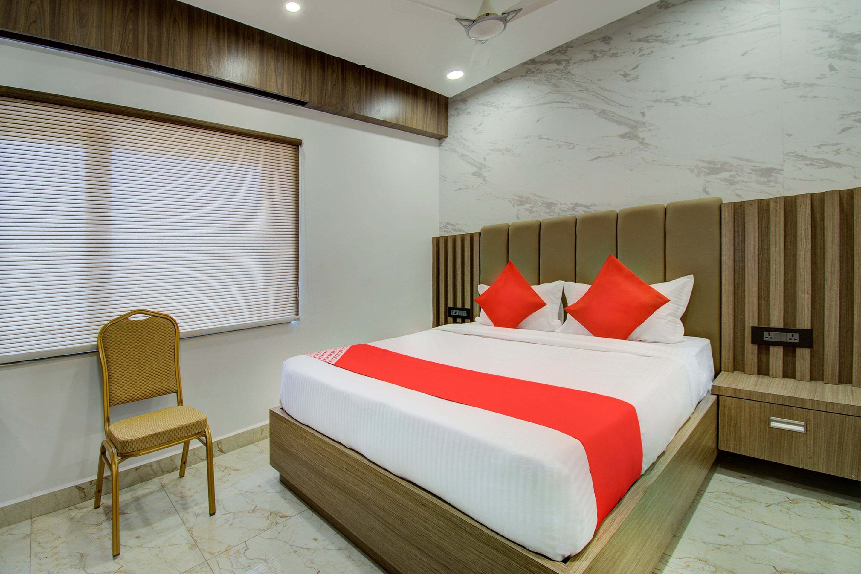 A hotel room with a large bed, a wooden nightstand, a chair, and a window with blinds.
