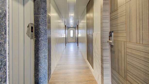 A long, narrow hallway with a marble floor and wooden panel walls. - Capital O 23031 V Hotel (Penumuluru)