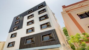 A modern multi-story building with a flat roof, large windows, and a mix of vertical and horizontal lines in the facade. - Capital O 23031 V Hotel (Penumuluru)