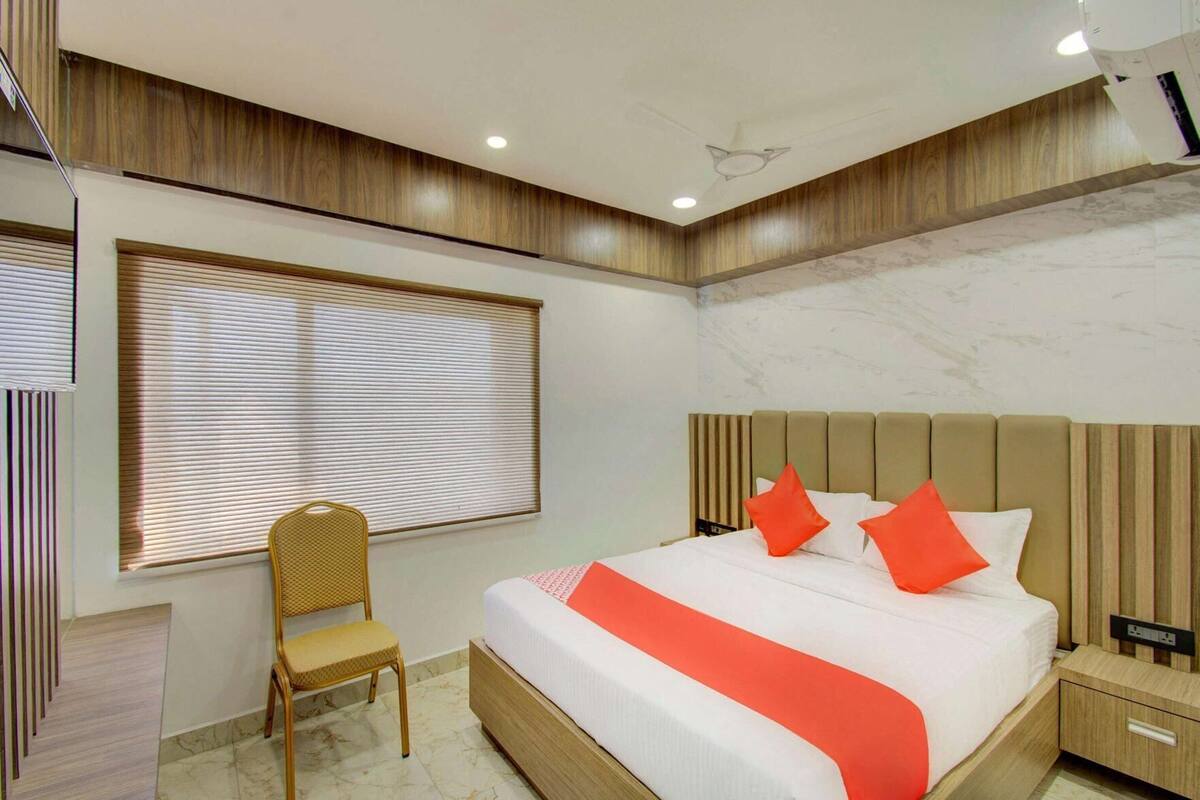 Een moderne slaapkamer met een bed, een stoel, een nachtkastje en een raam met jaloezieën.