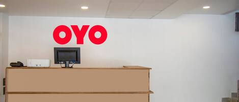 Egy tágas recepción található egy nagy „OYO” felirattal ellátott tábla, egy síkképernyős televízió és egy recepciós pult.