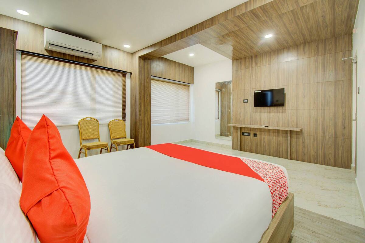 Een moderne hotelkamer met een groot bed, twee stoelen, een televisie en een airconditioning.