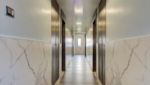 A long, narrow hallway with marble walls and a wooden floor, leading to a door at the end. - Capital O 23031 V Hotel (Penumuluru)