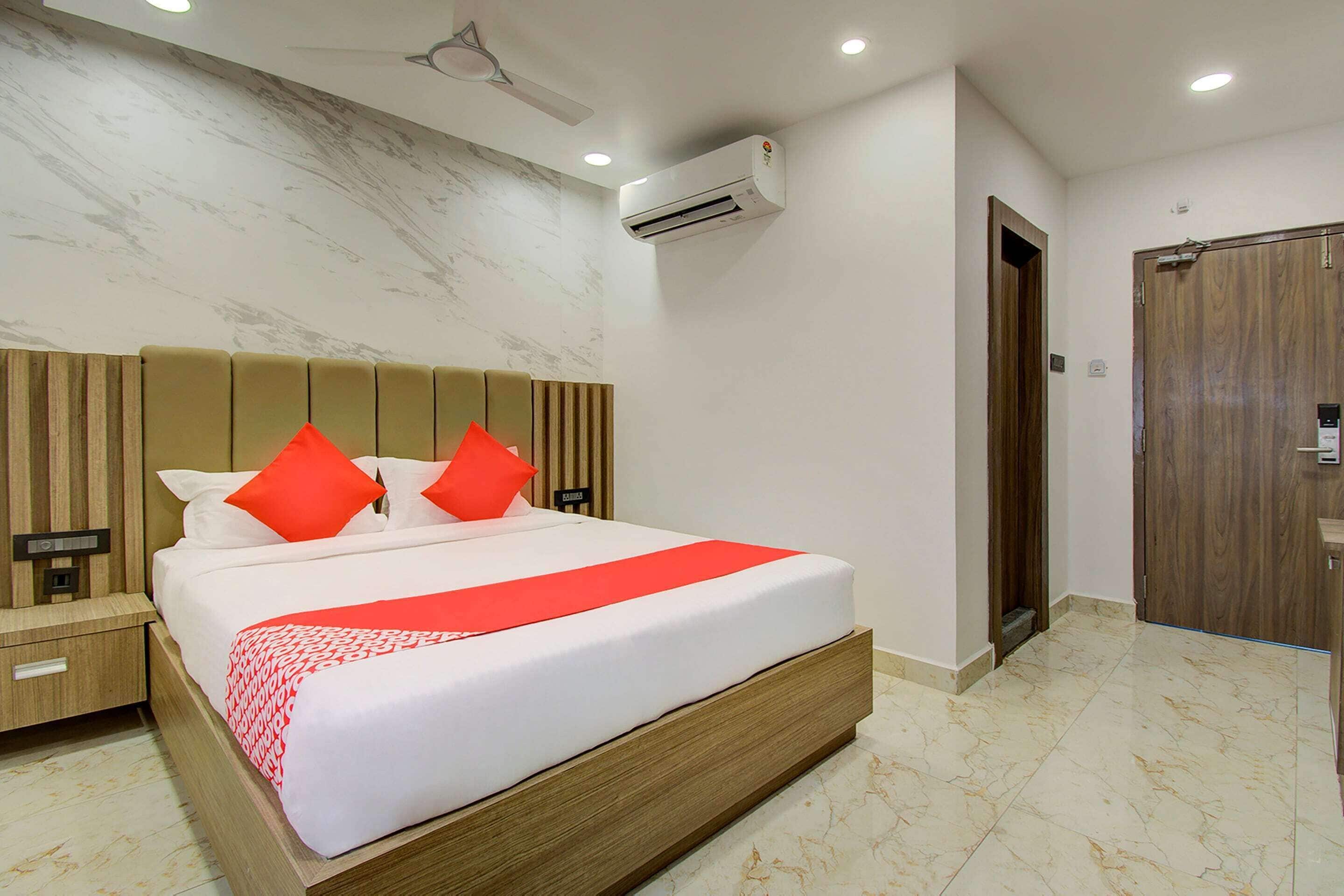 Habitación de hotel con una cama grande, cabecera de madera y almohada roja decorativa.