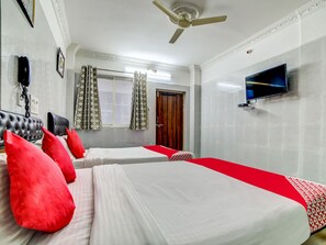 A hotel room with two beds, a ceiling fan, a TV, and a window with curtains.
