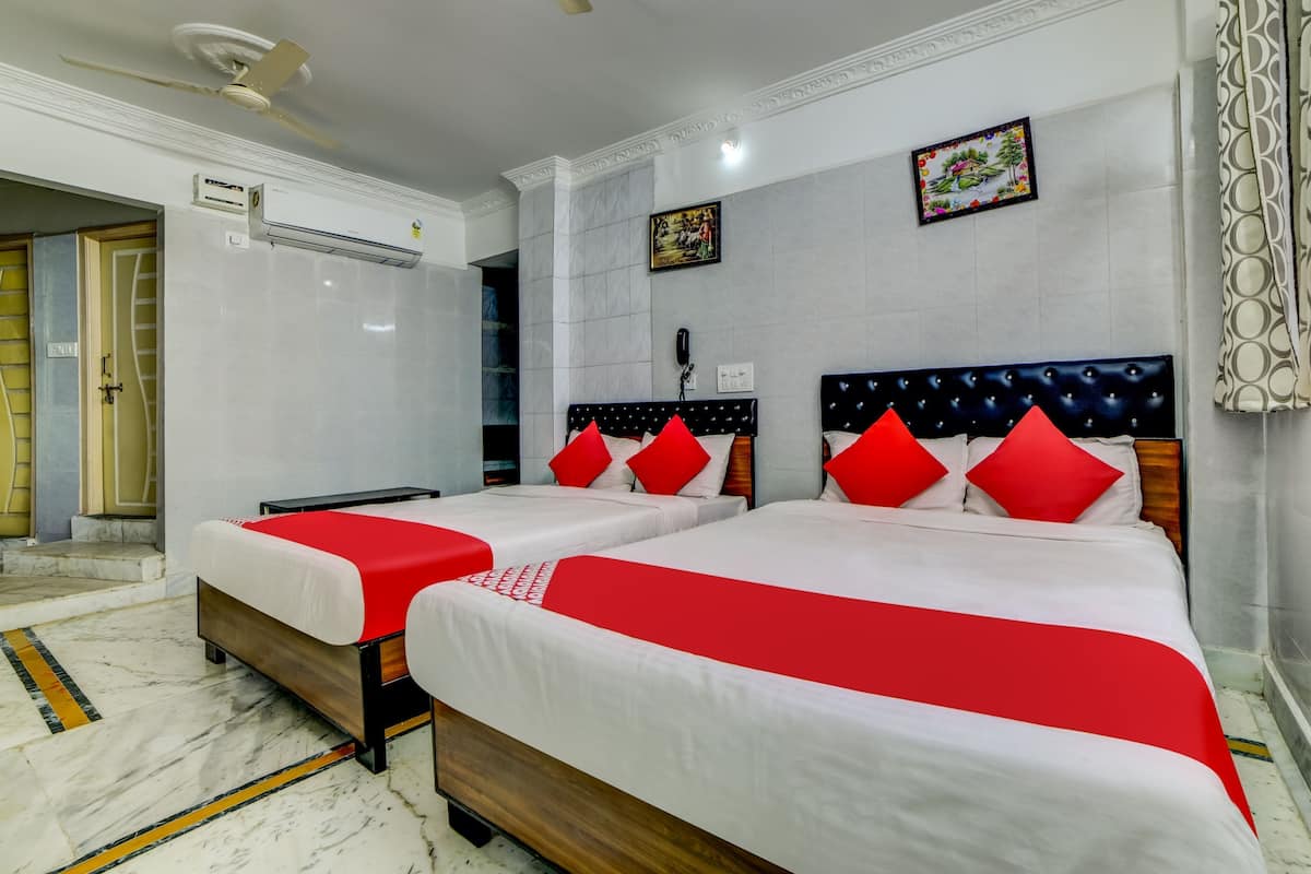 Quarto de hotel com duas camas, um ventilador de teto, aparelho de ar condicionado, telefone e um quadro decorativo na parede.