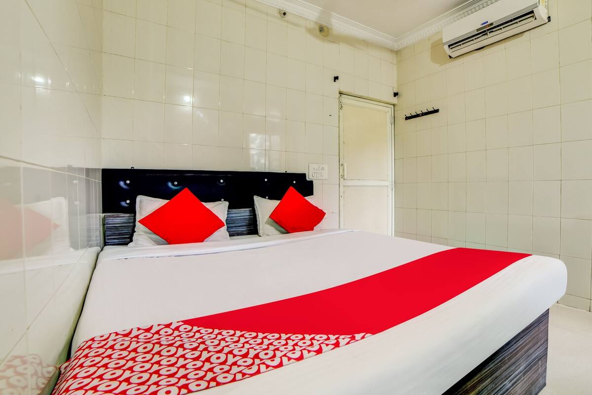 Quarto de hotel com cama, paredes revestidas de azulejos brancos, cabeceira preta e edredom com padrão vermelho e branco.