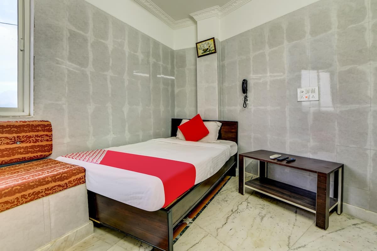 Quarto de hotel com cama, mesa de cabeceira, telefone e interruptor de luz na parede.