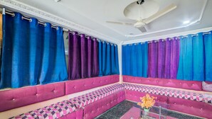 A room with a sectional sofa, a ceiling fan, and patterned curtains. - OYO 29087 Hotel Golden Pride (Hyderabad)