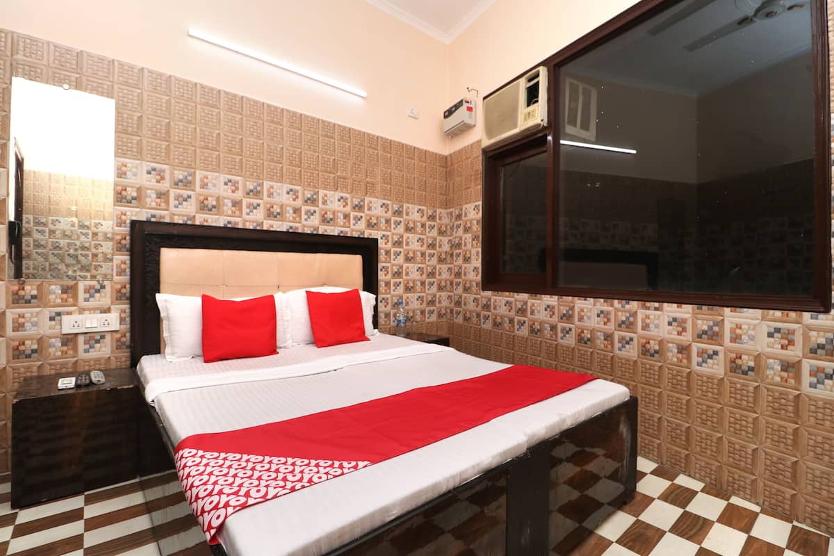 Ein Hotelzimmer mit einem Bett, einem Nachttisch, einer roten Tagesdecke, einem karierten Boden und Wandverkleidung mit Muster.