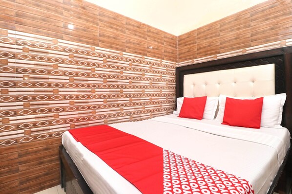 A hotel room with a patterned wall, a tufted headboard, and a red throw blanket.