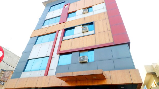 Ein mehrstöckiges Gebäude mit modernem architektonischen Design, das Glas- und Holzverkleidungen kombiniert und mehrere Klimaanlagen an der Fassade zeigt.