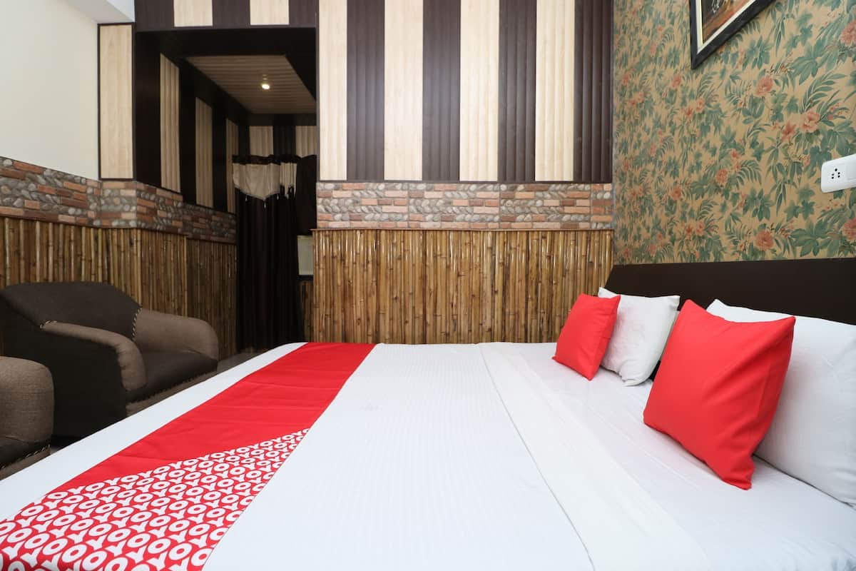 A hotel room with a bed, a red and white patterned bedspread, a headboard, and a wall with vertical stripes and a floral wallpaper section.