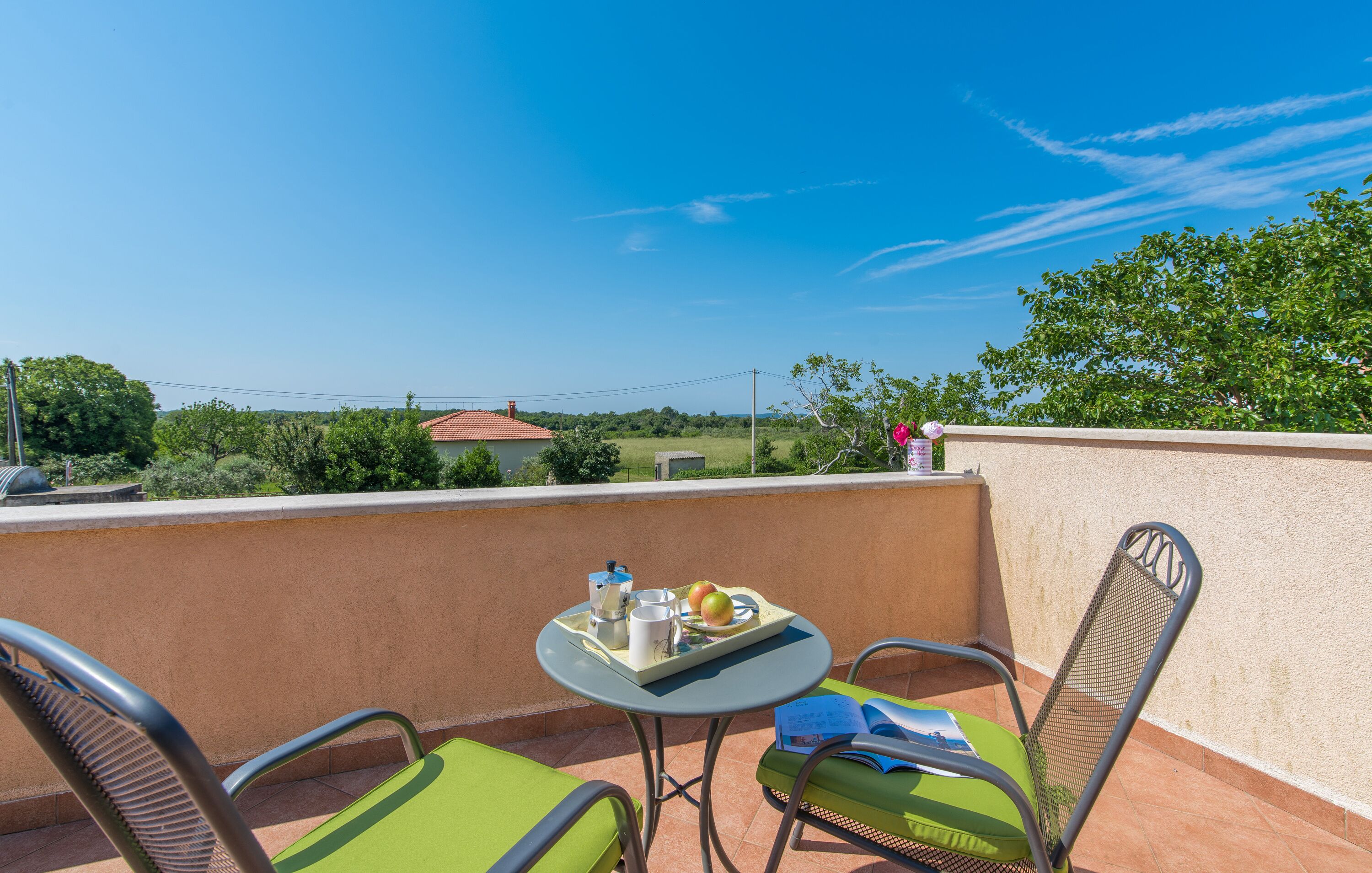 A balcony with a table set for two, chairs, and a view of the countryside.