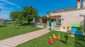 A house with a paved driveway, a play area with toys, and a garden.