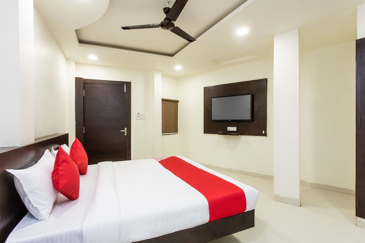A hotel room with a bed, a ceiling fan, a mounted TV, and a door.