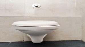 Des toilettes dans une salle de bain avec un mur blanc et un sol noir.