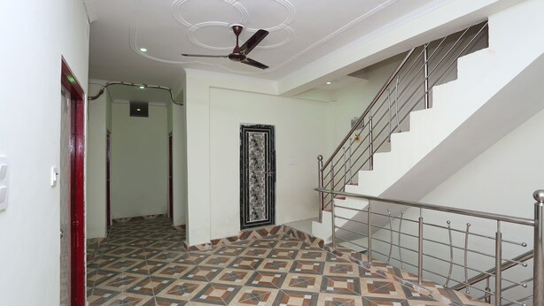Un couloir doté d’un revêtement de sol à motifs, d’un ventilateur de plafond, d’un escalier avec une rampe en métal et d’une porte ornée d’un cadre décoratif.
